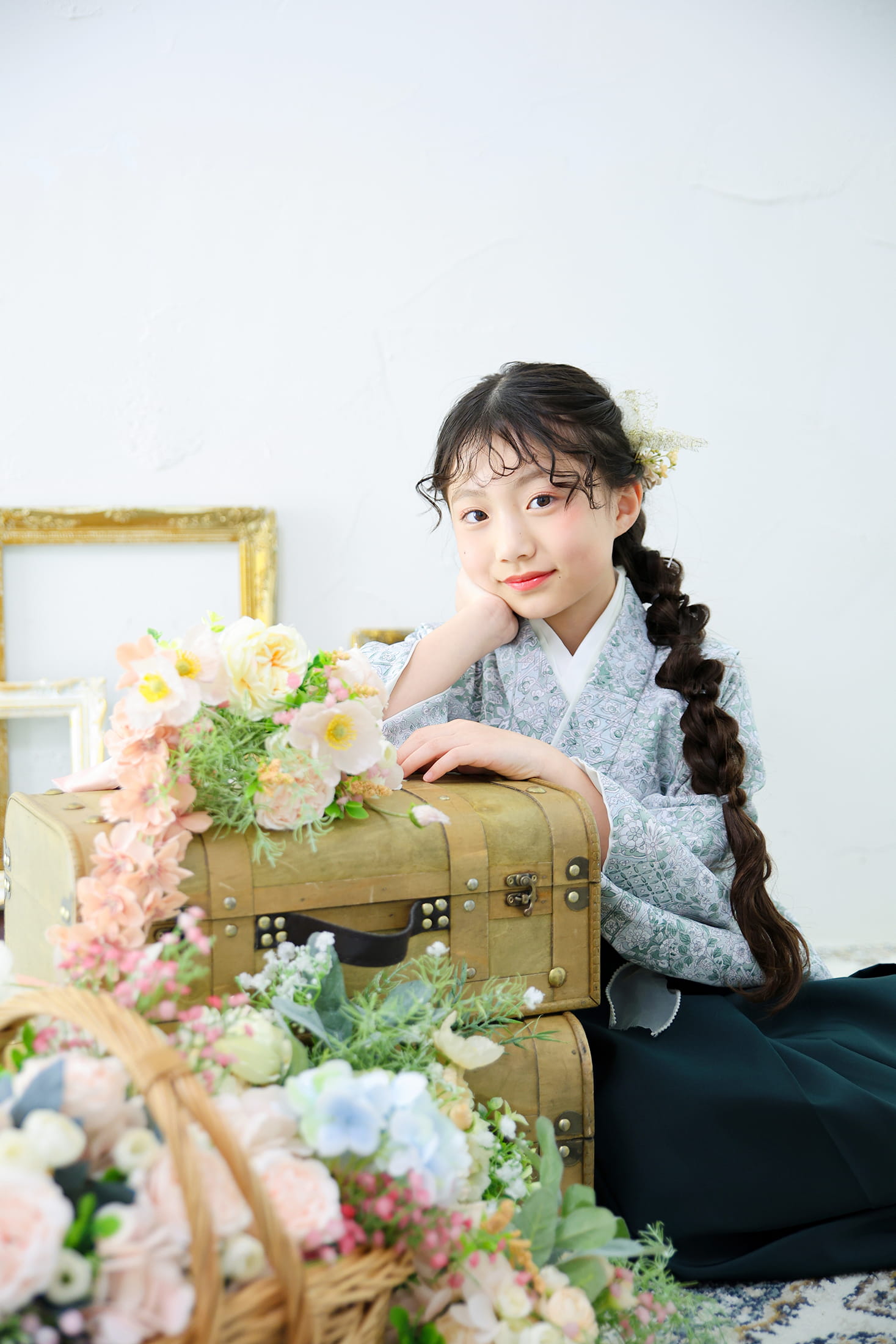 袴姿の女性が花に囲まれたアンティークのトランクに寄り添う写真