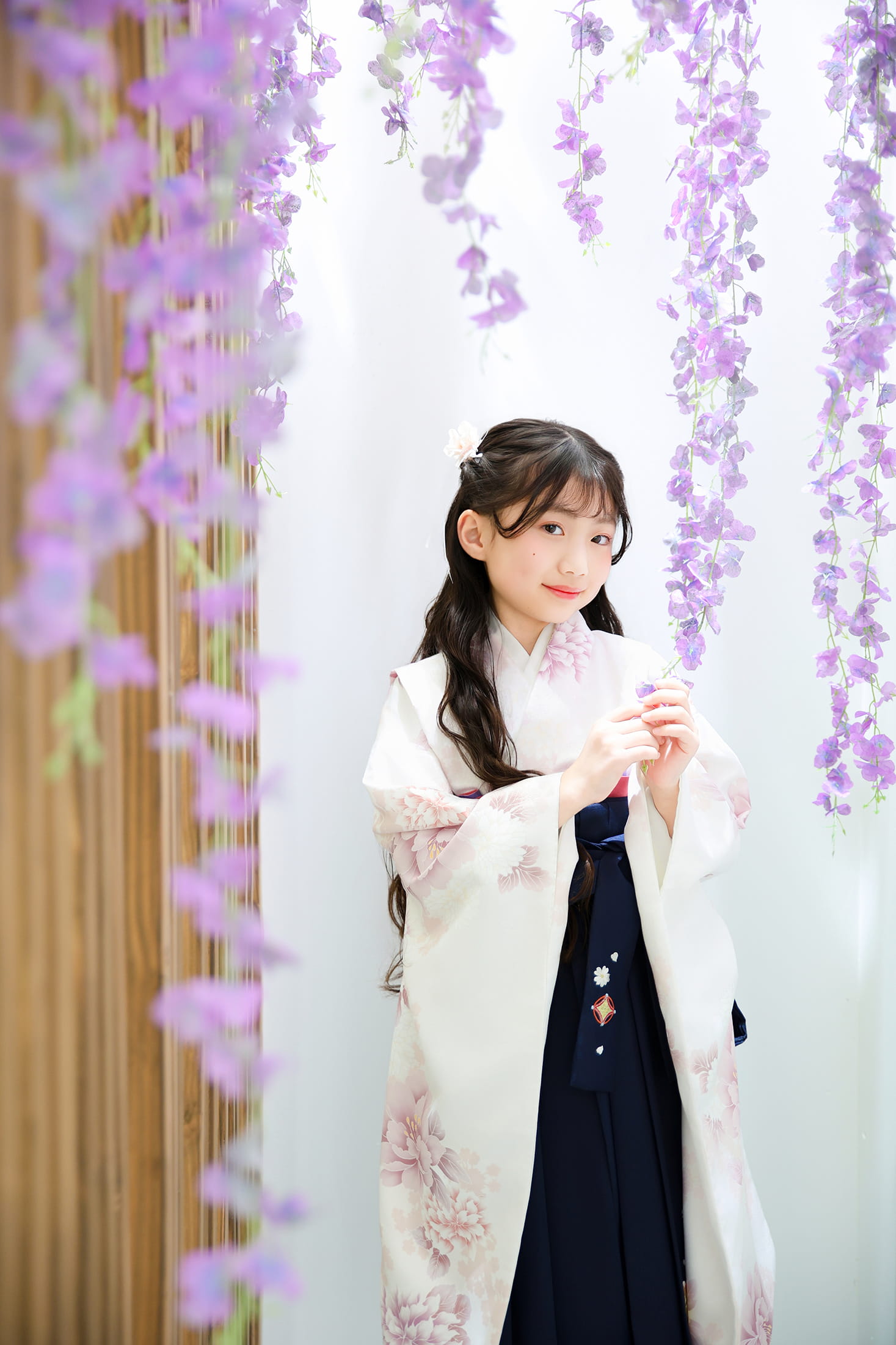 藤の花が垂れ下がる中で白い着物と紺色の袴を着た女性