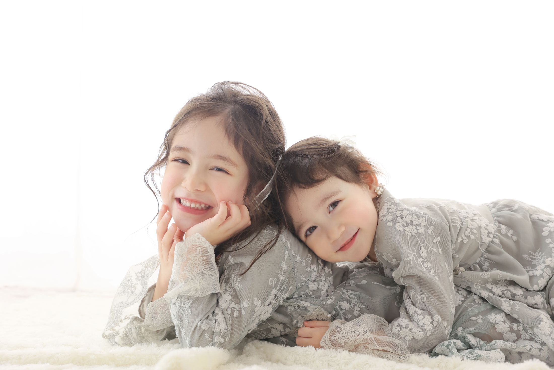 お揃いのドレス衣装を着た7歳の女の子と5歳の女の子。シンプルなスタジオで姉妹で撮影している七五三の写真。