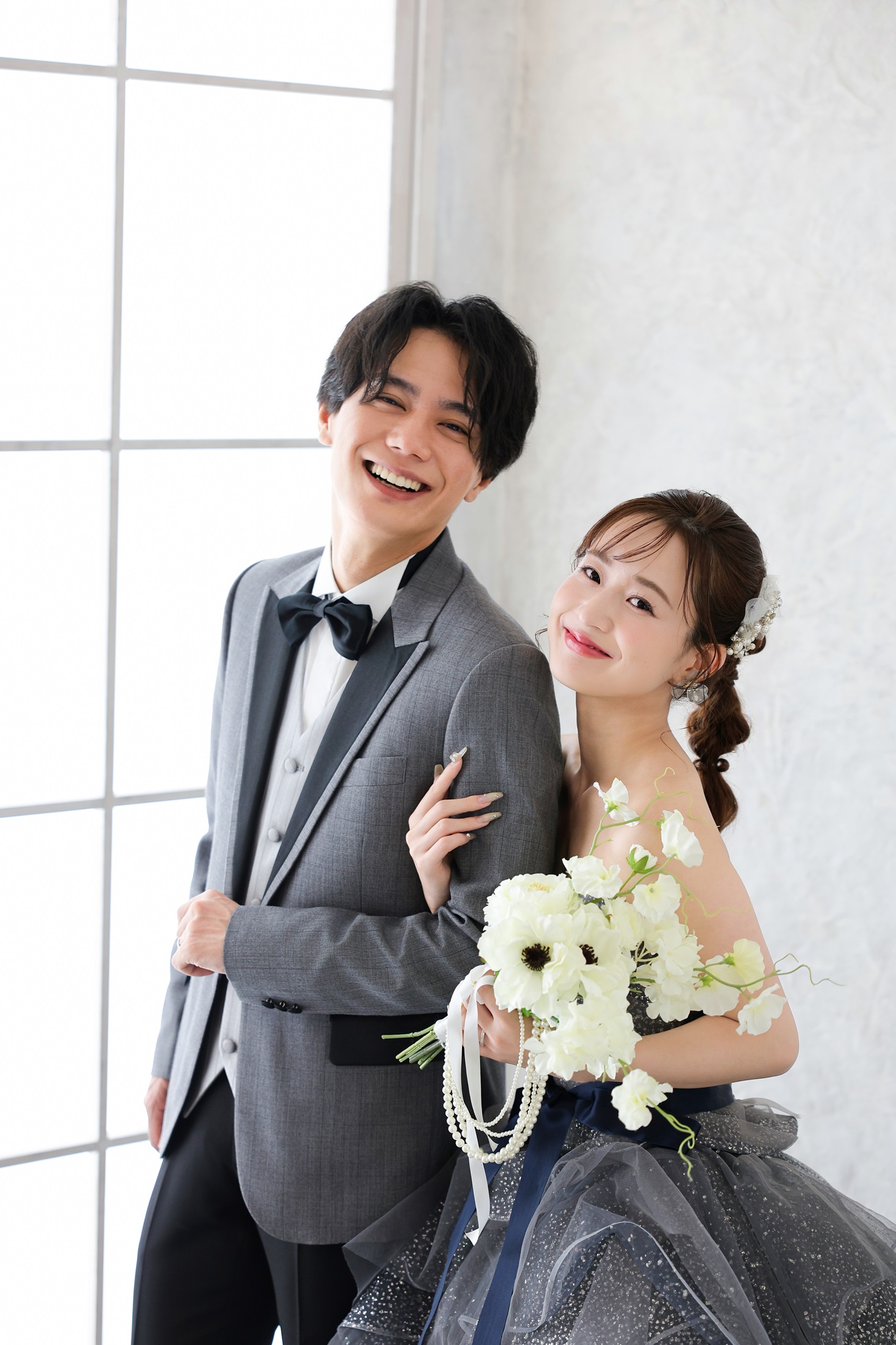 カラードレスとタキシードでフォトウェディングの撮影をする新郎新婦様。大きな窓から降り注ぐ光に包まれ撮影をする新郎新婦様。撮影店舗：しんかな大阪南店 住所：大阪府堺市北区長曽根町3069-7