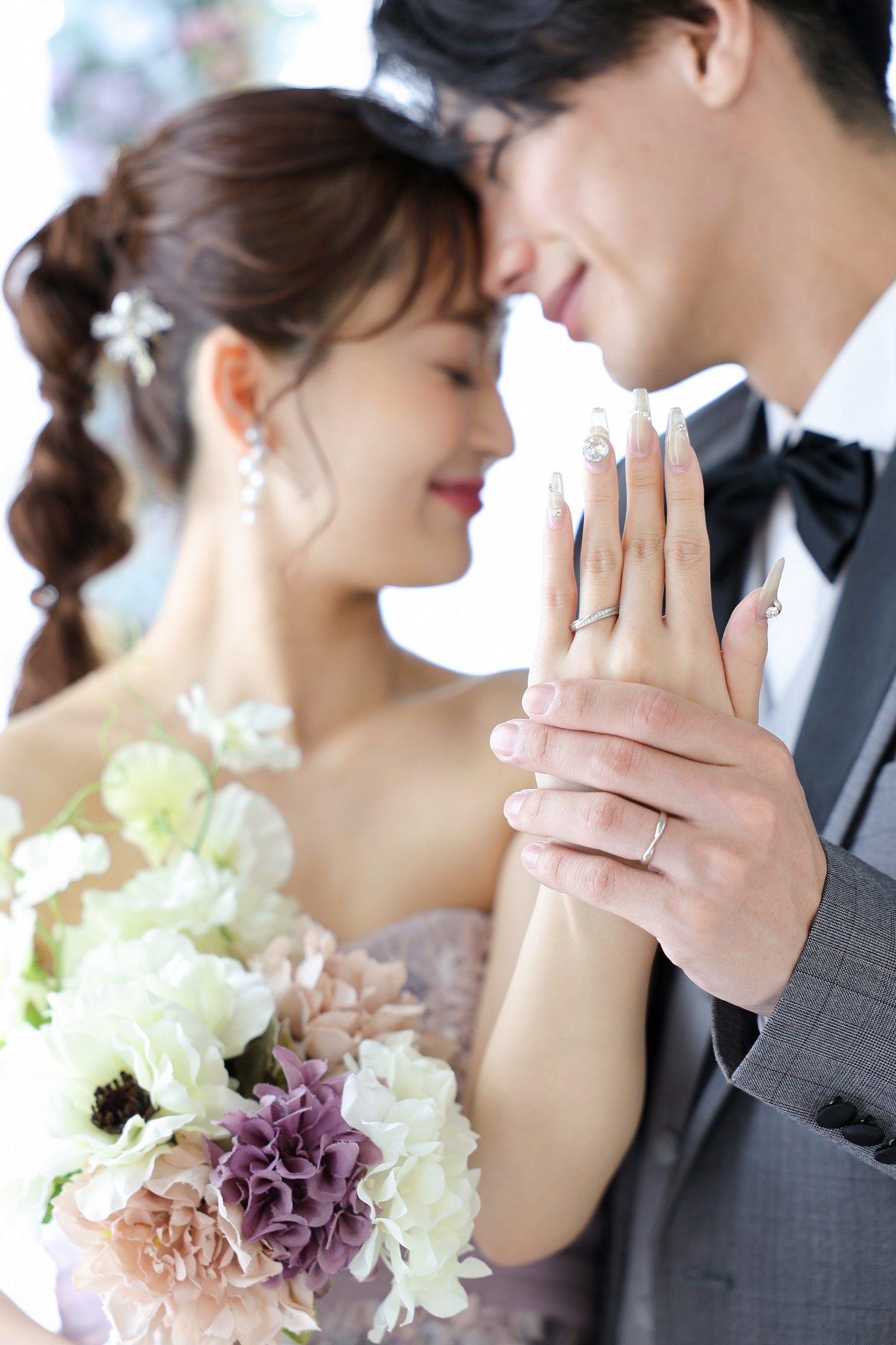 カラードレスとタキシードでフォトウェディングの撮影をする新郎新婦様。淡い色のブーケを抱える新婦様と新郎様のお手元にフォーカスして撮影している写真。撮影店舗：しんかな大阪南店 住所：大阪府堺市北区長曽根町3069-7