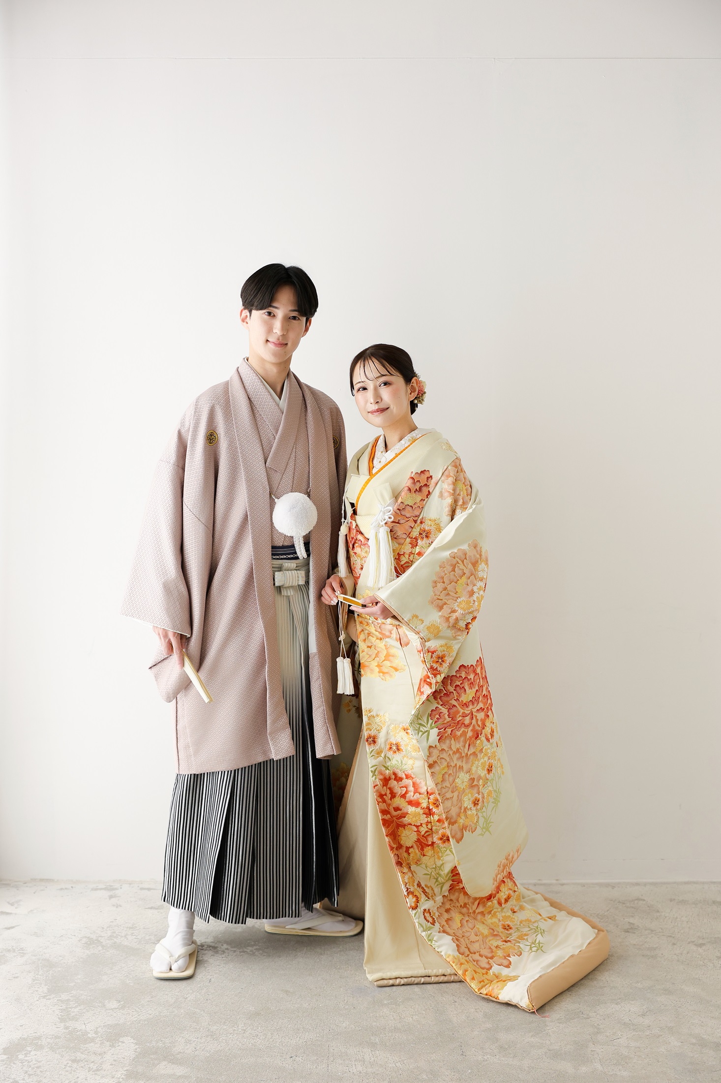 色打掛と袴でフォトウェディングの撮影をする新郎新婦様。真っ白な壁を背景に、オレンジ色が映える色打掛の新婦様と新郎様の全身を撮影している写真。撮影店舗：しんかな大阪南店 住所：大阪府堺市北区長曽根町3069-7