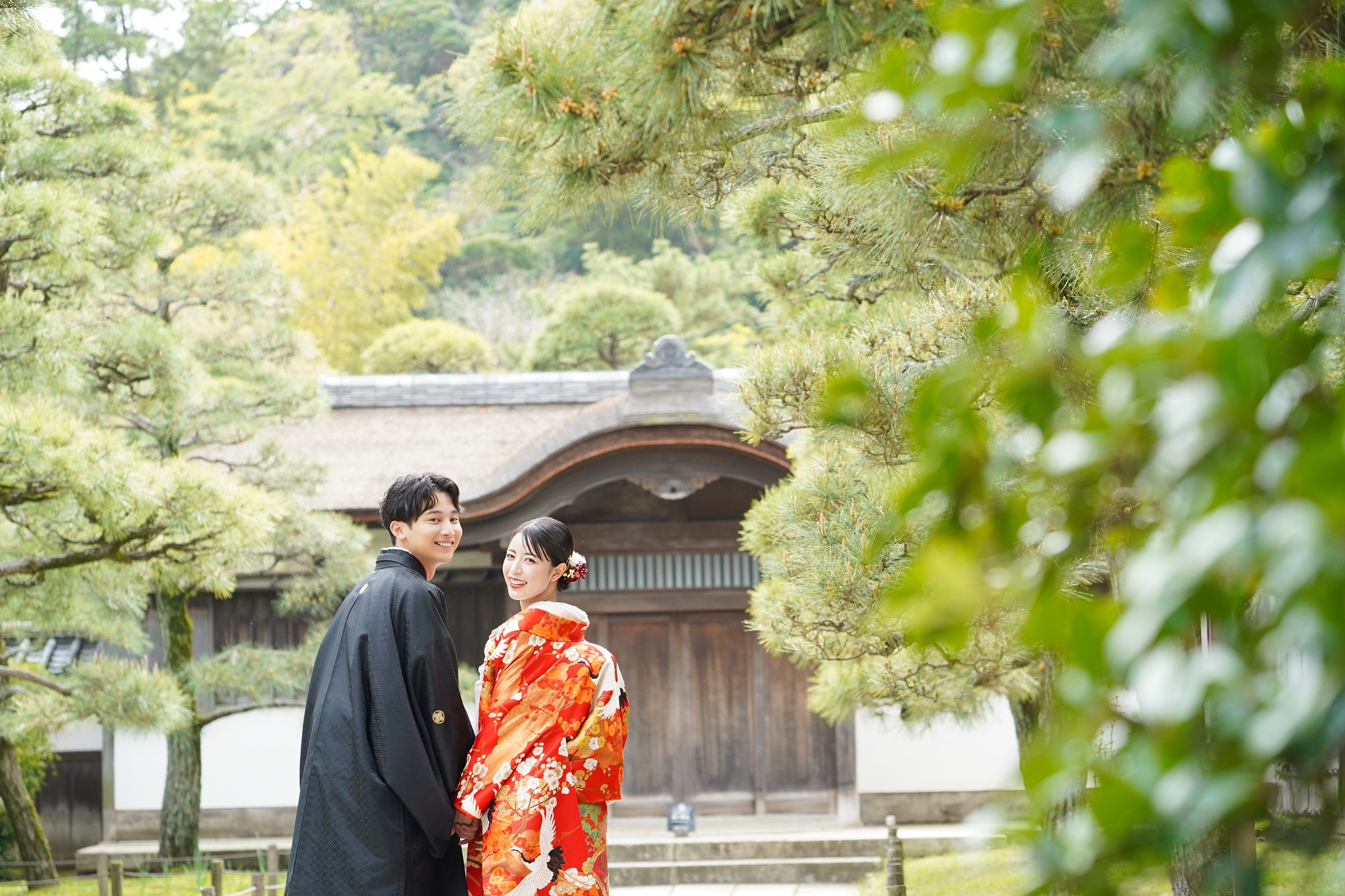 三渓園の日本庭園で和装を着て結婚式の前撮りをする新郎様と新婦様。赤の色打掛が王道の美しさで庭園の雰囲気ともマッチしている 。撮影：STUDIOARC
