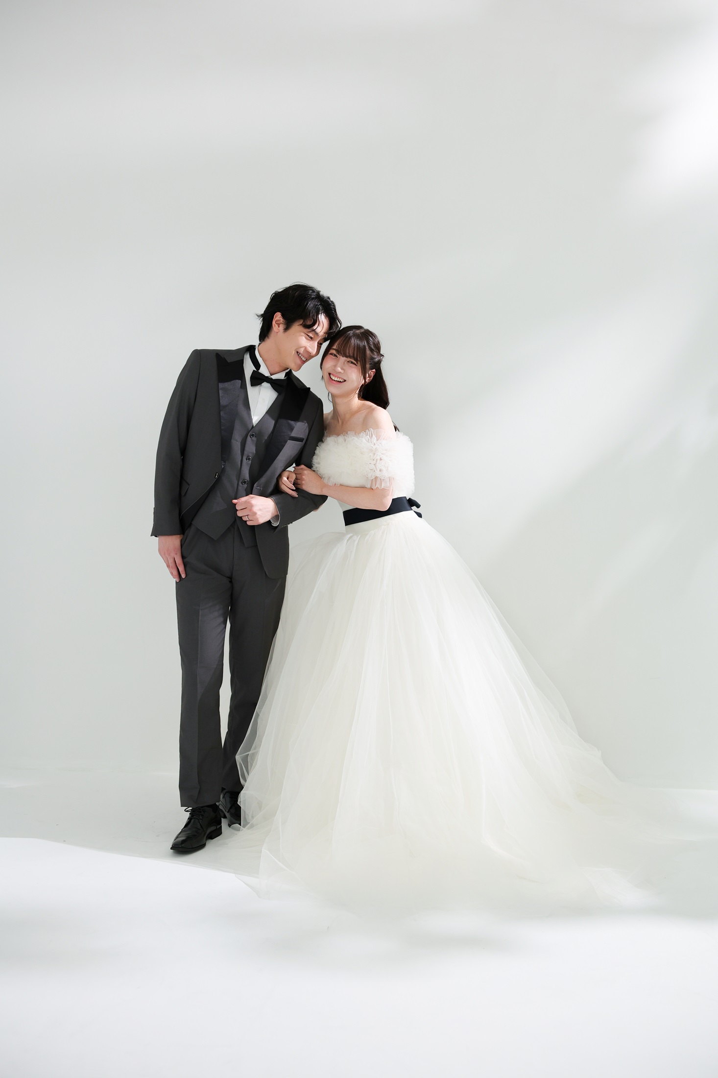 ウェディングドレスとタキシードでフォトウェディングの撮影をする新郎新婦様。柔らかな光が差し込む真っ白の壁を背景に撮影している写真。撮影店舗:ららテラスHARUMI FLAG店 住所:東京都中央区晴海五丁目2番31号 ららテラス HARUMI FLAG 3階