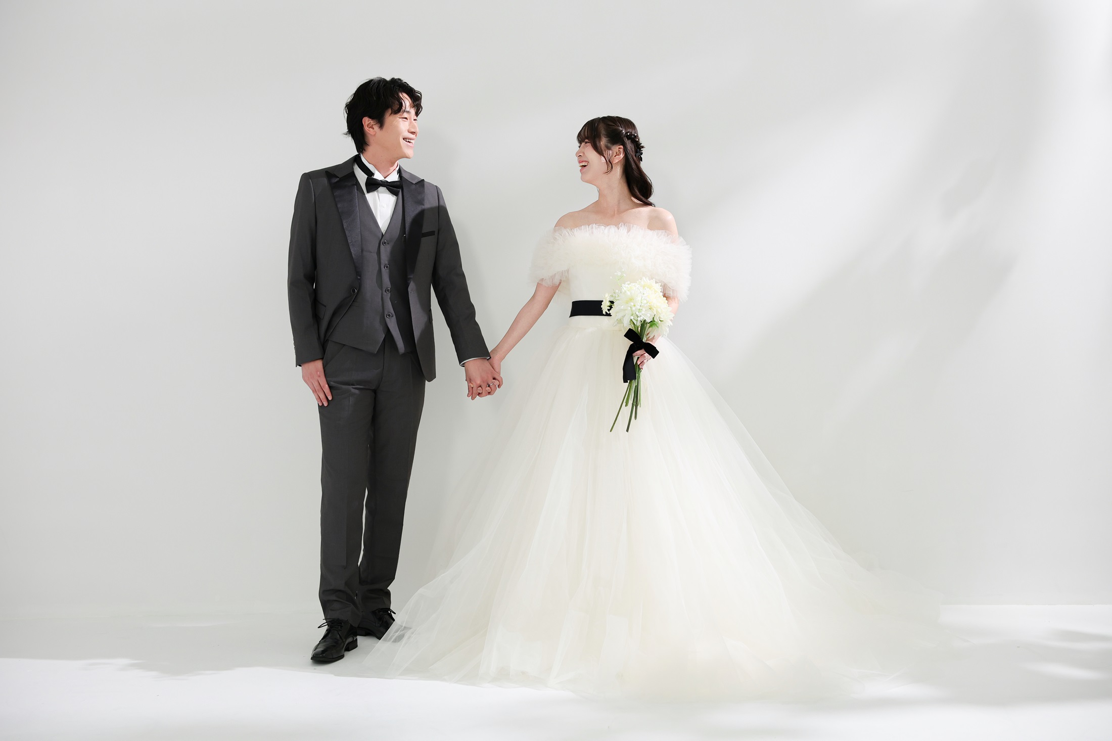 ウェディングドレスとタキシードでフォトウェディングの撮影をする新郎新婦様。柔らかな光が差し込む真っ白の壁を背景に撮影している写真。撮影店舗:ららテラスHARUMI FLAG店 住所:東京都中央区晴海五丁目2番31号 ららテラス HARUMI FLAG 3階