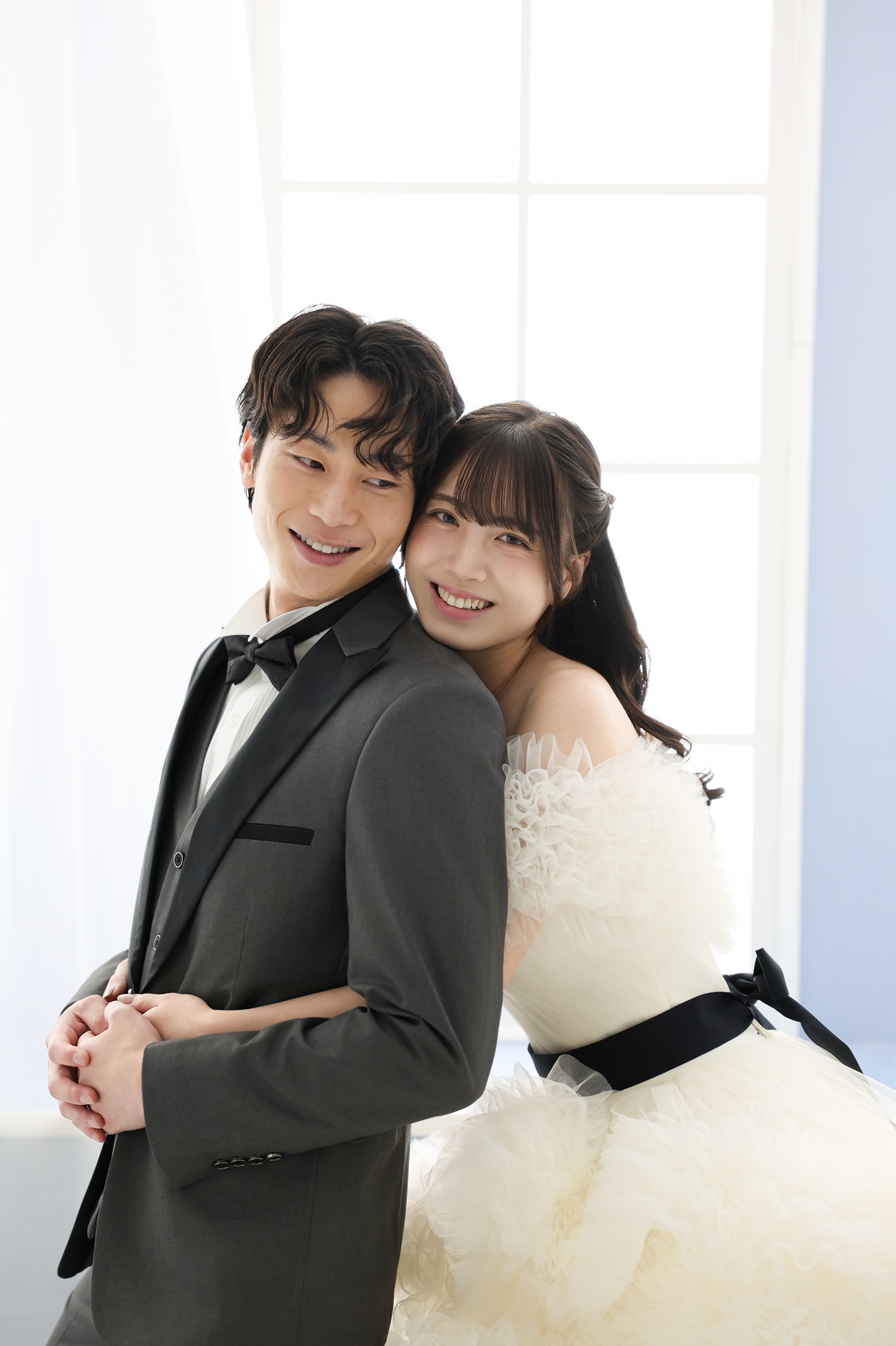 ウェディングドレスとタキシードでフォトウェディングの撮影をする新郎新婦様。柔らかな光に包まれる中、新婦様が後ろから新郎様に抱きつき笑顔の様子を撮影している写真。 撮影店舗:ららテラスHARUMI FLAG店 住所:東京都中央区晴海五丁目2番31号 ららテラス HARUMI FLAG 3階