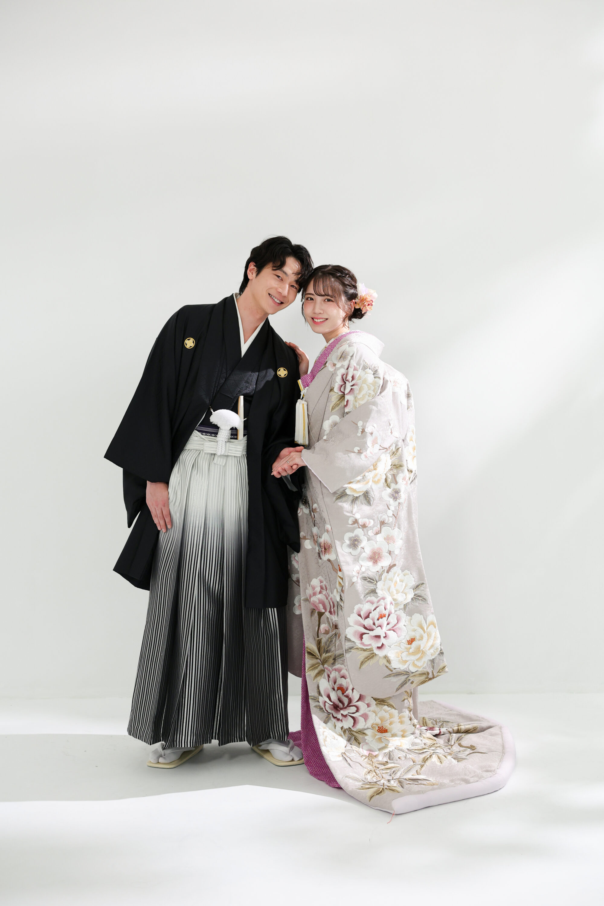 色打掛と袴でフォトウェディングの撮影をする新郎新婦様。柔らかな光が注ぐ真っ白の壁を背景に、淡い色合いの色打掛が映える新婦様と新郎様を撮影している写真。撮影店舗:ららテラスHARUMI FLAG店 住所:東京都中央区晴海五丁目2番31号 ららテラス HARUMI FLAG 3階