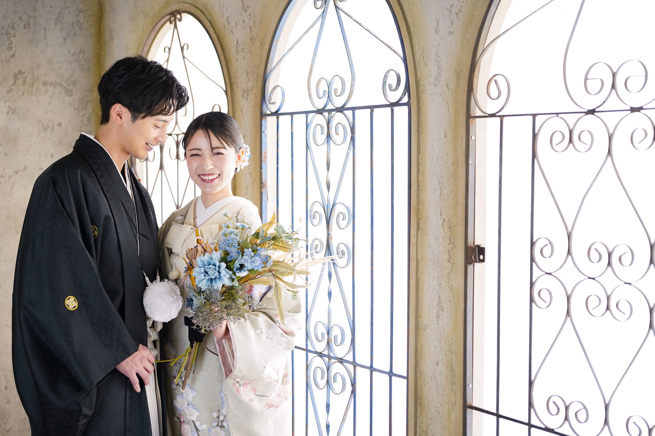 結婚式の前撮り撮影をする紋付き袴を着た新郎様と色打掛を着た新婦様。アンティーク家具の背景の中で笑顔で撮影している写真。 撮影店舗：STUDIOARC横浜店 住所：神奈川県横浜市中区山下町84-5 メトロタワー山下町 4F