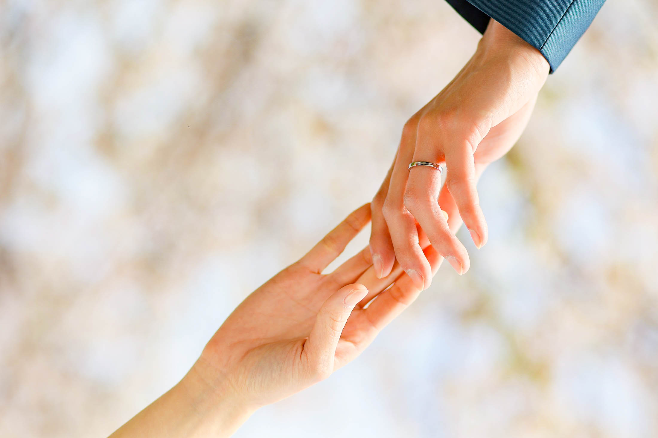 神戸ハーバーランドでフォトウエディング撮影。新郎様と新婦様が桜の木をバックに結婚指輪をはめた手を繋いでいるアップ写真。結婚の記念写真撮影