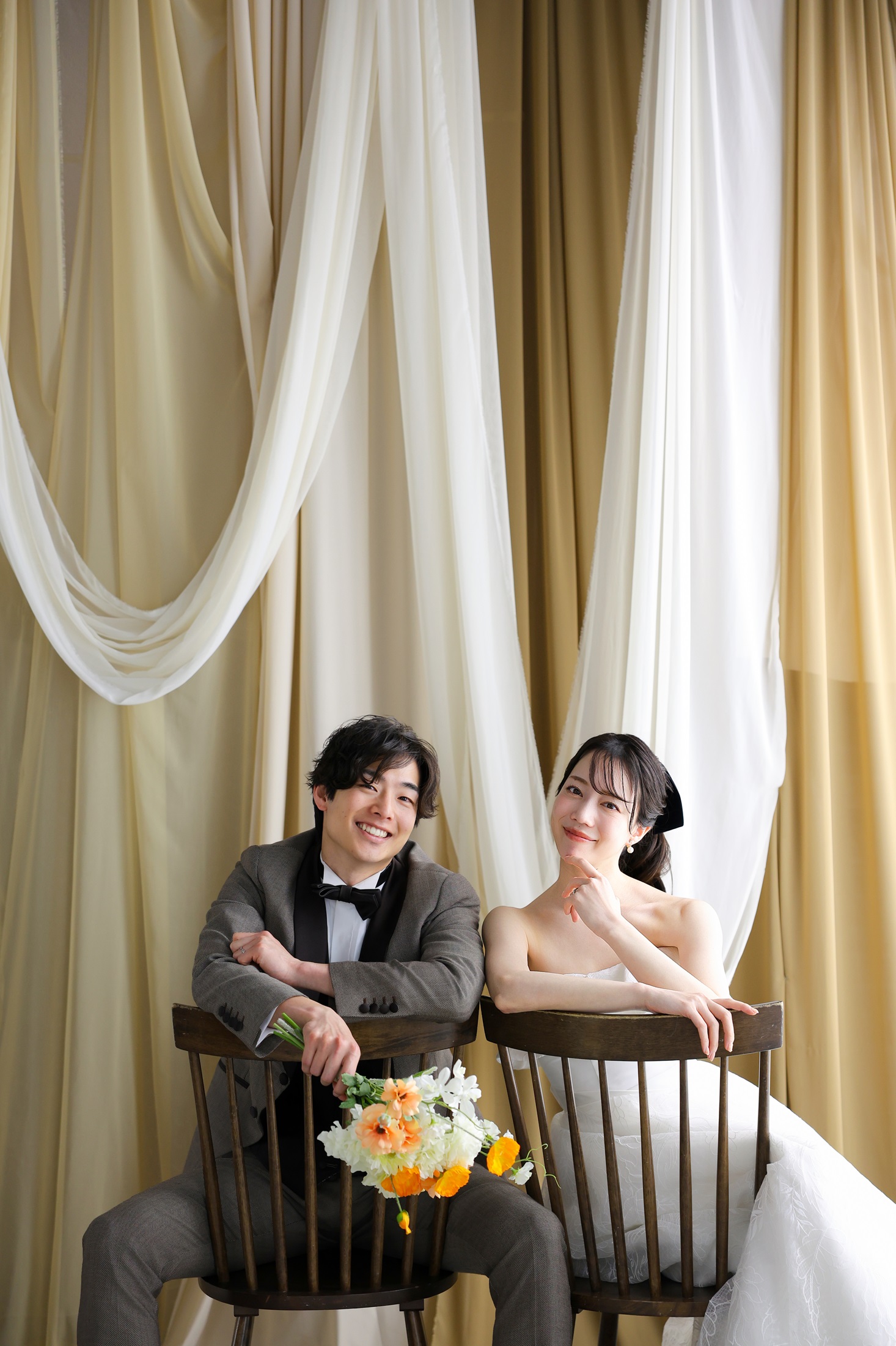 ウェディングドレスとタキシードでフォトウェディングの撮影をする新郎新婦様。クラシカルな椅子の背もたれを前に向け、二人で座っている新郎新婦様を撮影したスタイリッシュな写真。撮影店舗：神戸ハーバーランド店 住所：兵庫県神戸市中央区東川崎町1-5-5 ハーバーランド煉瓦倉庫