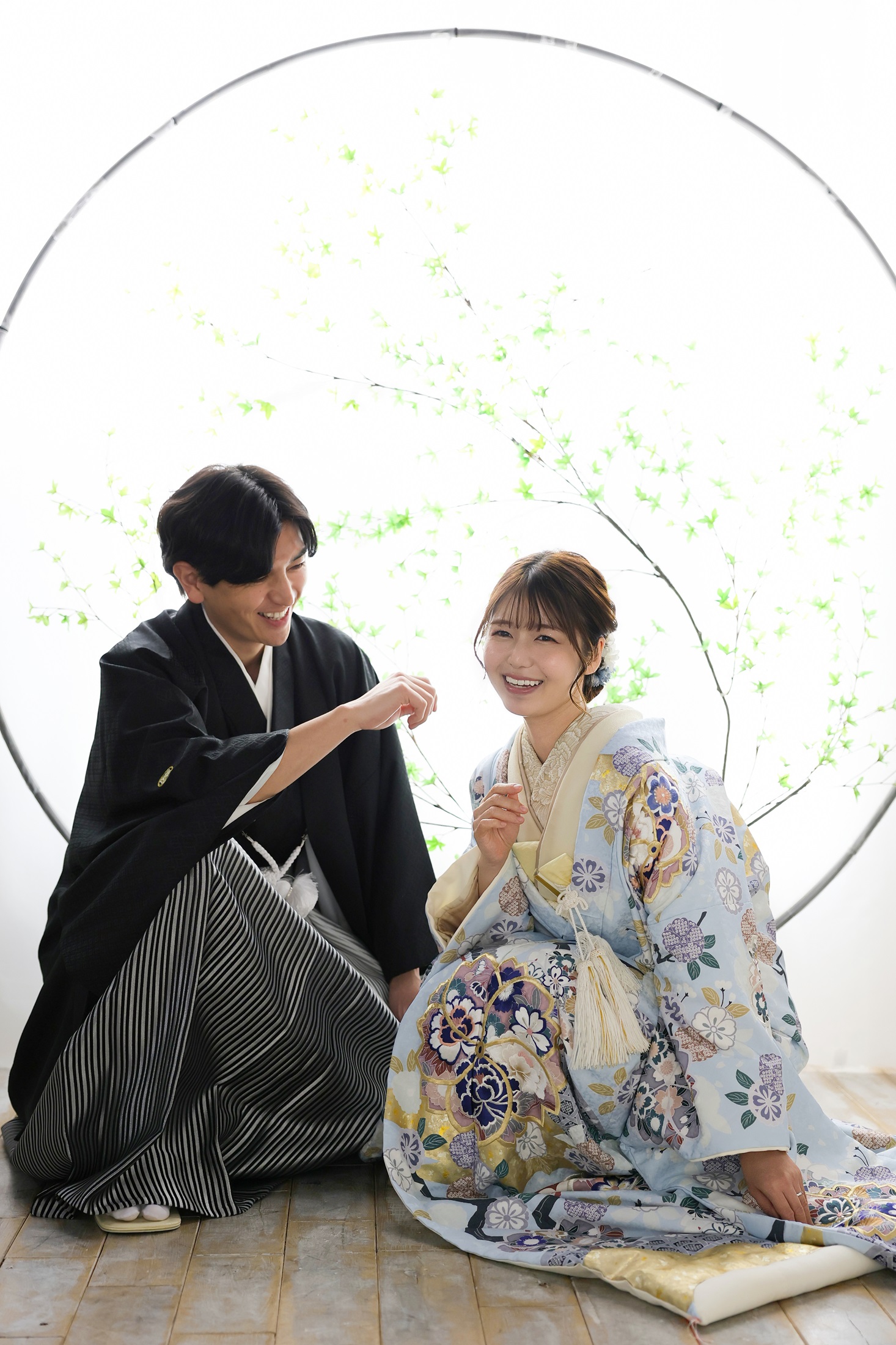 色打掛と袴でフォトウェディングの撮影をする新郎新婦様。明るい光が降り注ぐ丸窓から、庭園の緑が切り取られたような和の景色を背景に、座って撮影している新郎新婦様を撮影した写真。撮影店舗：神戸ハーバーランド店 住所：兵庫県神戸市中央区東川崎町1-5-5 ハーバーランド煉瓦倉庫