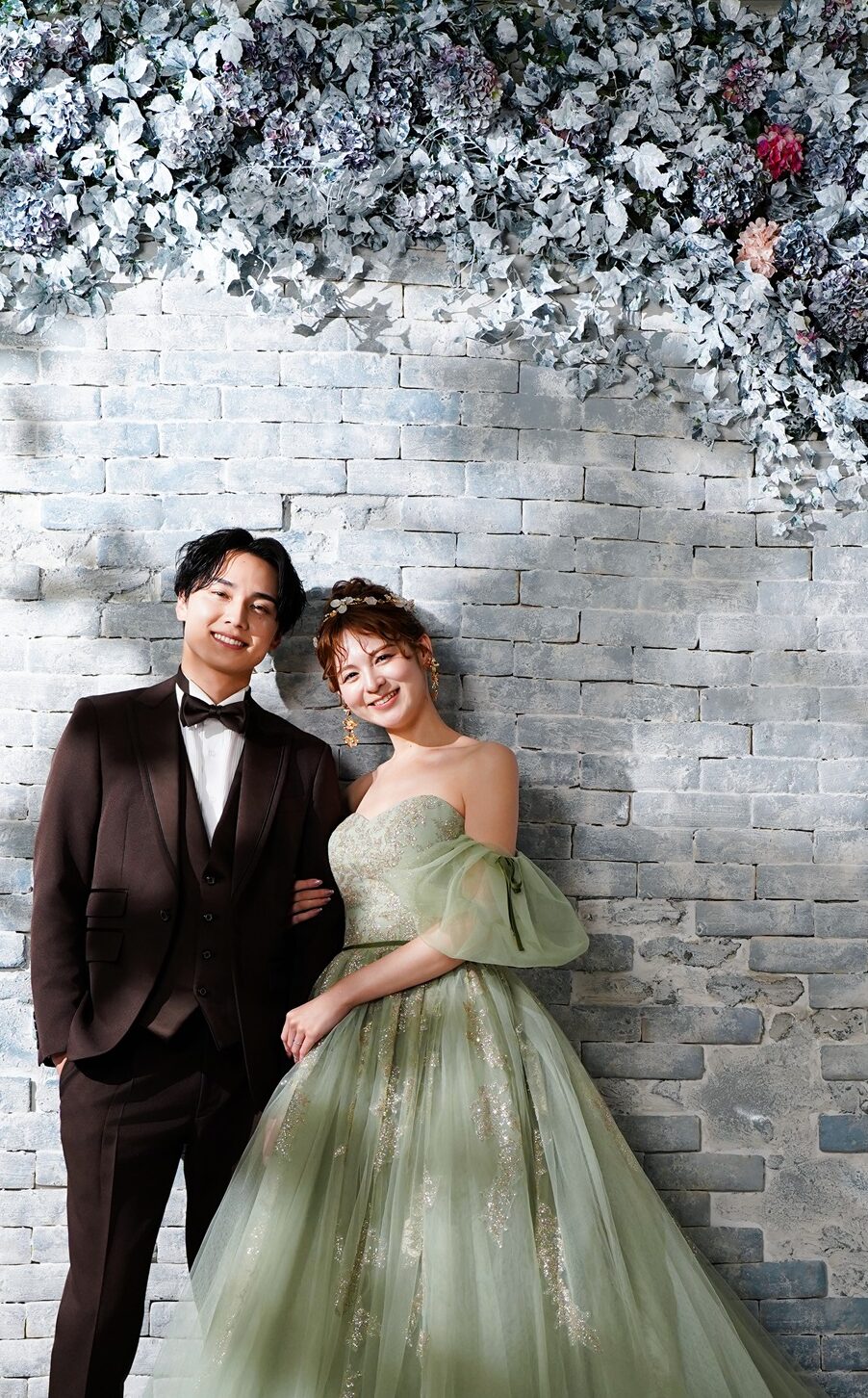 カラードレスとタキシードでフォトウェディングの撮影をする新郎様と新婦様。ナチュラルな花の背景で撮影している写真。 撮影店舗：STUDIOARC横浜店 住所：神奈川県横浜市中区山下町84-5 メトロタワー山下町 4F