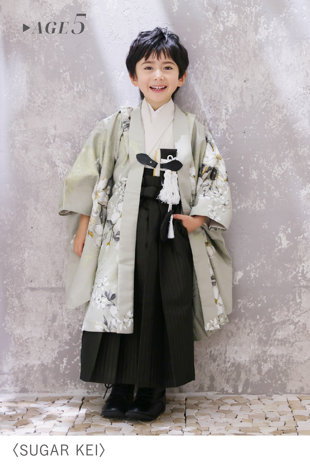 「SUGAR KEI」の5歳男の子用衣装を着用し、グレーの花柄羽織と縞模様の黒袴、白扇子でおしゃれにコーディネートした七五三着物スタイル