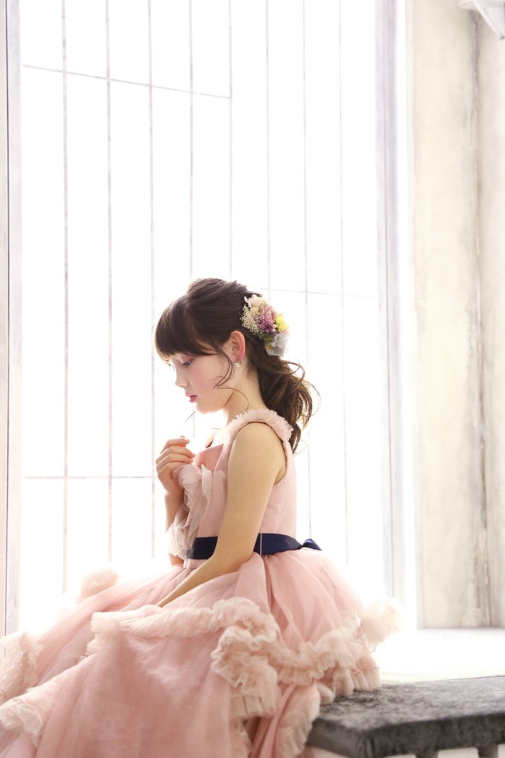 ピンクのドレスを着て窓辺に座り、横顔を見せる七五三の女の子の写真