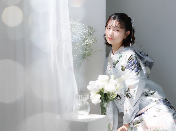 白い花が飾られた窓辺でブランド振袖を着て微笑む女性の写真