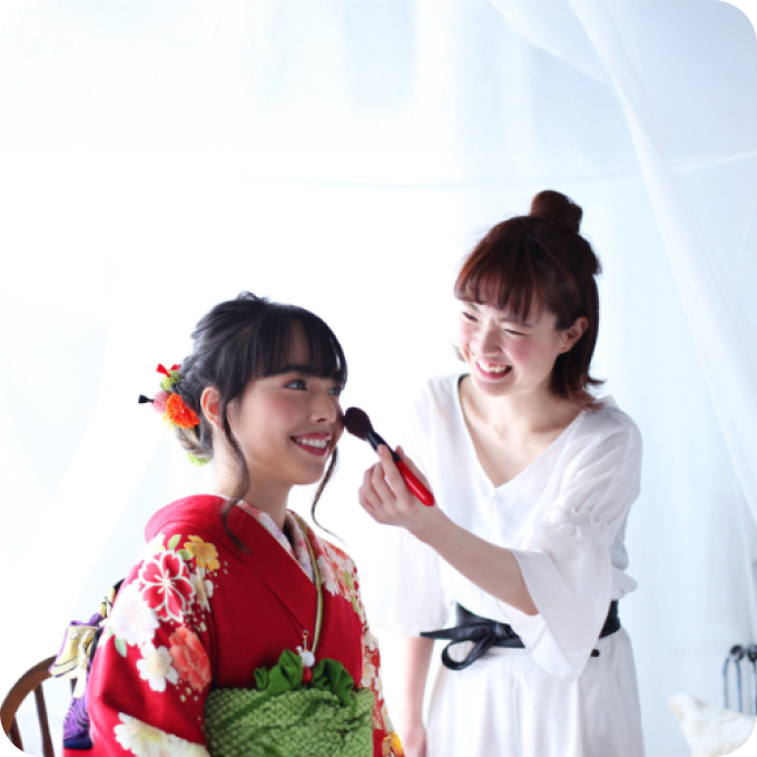 赤い花柄の着物を着た女の子にヘアメイクを施すスタッフ。撮影に合わせたヘア・メイクの提案風景
