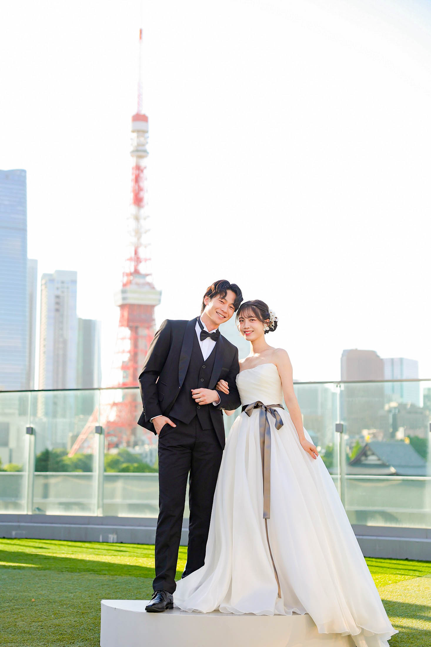 STUDIO ARC 芝Parkside STUDIO店の芝生のある屋上にて撮影。タキシードを着た新郎様とウェディングドレスを着た新婦様が東京タワーをバックに頭を寄せ合って撮った写真。スタジオアーク芝 店舗住所:東京都港区芝2-1-28 芝アネックスビル1階