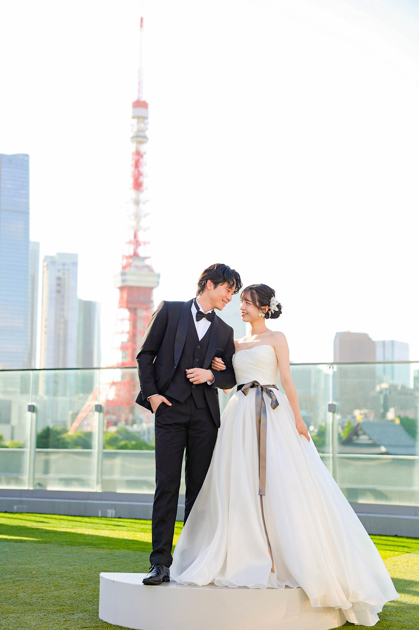 STUDIO ARC 芝Parkside STUDIO店の芝生のある屋上にて撮影。タキシードを着た新郎様とウェディングドレスを着た新婦様が東京タワーをバックに頭を寄せ合って撮った写真。スタジオアーク芝 店舗住所:東京都港区芝2-1-28 芝アネックスビル1階