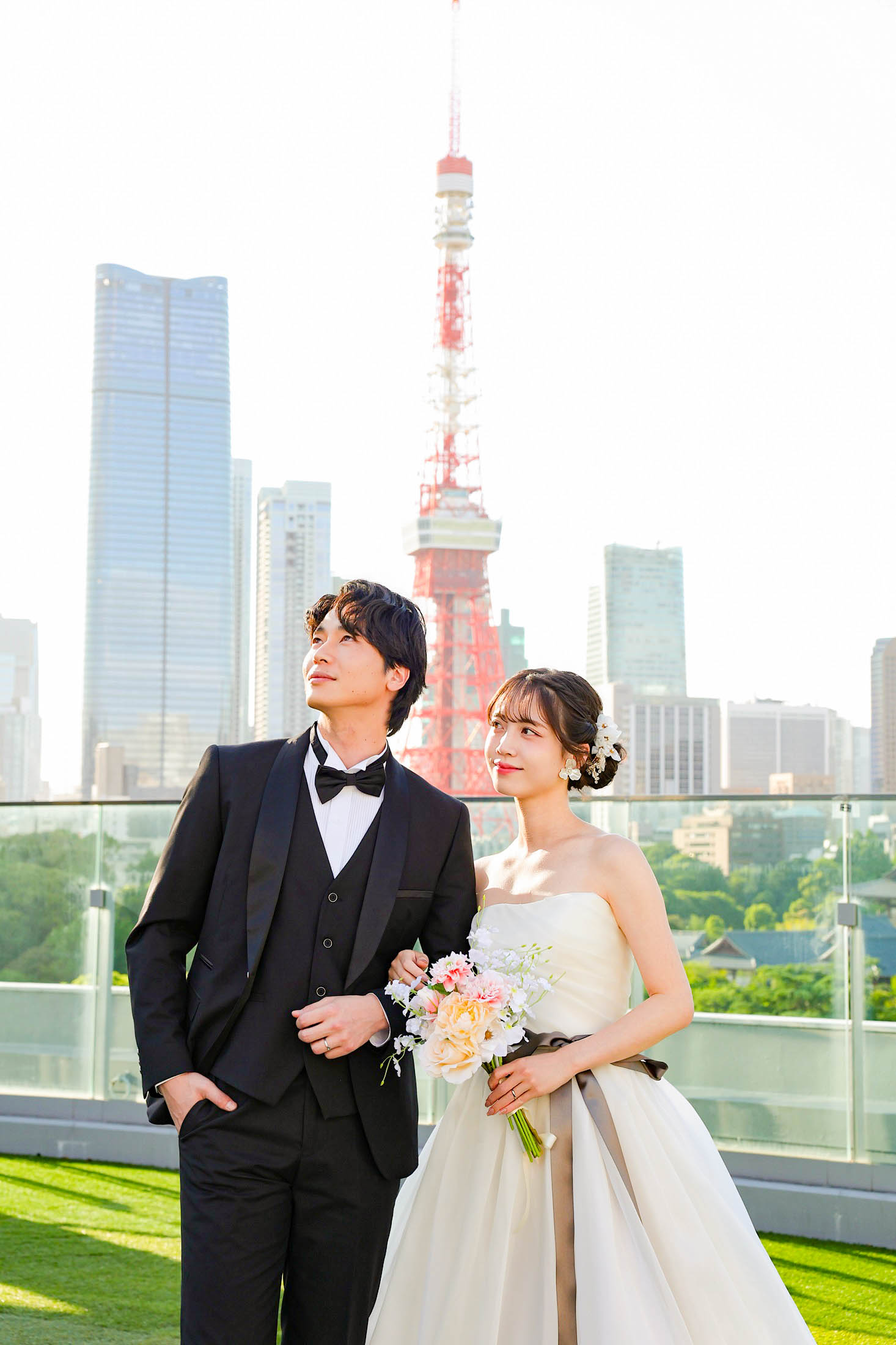 STUDIO ARC 芝Parkside STUDIO店の芝生のある屋上にて撮影。タキシードを着た新郎様とウェディングドレスを着てブーケを持った新婦様が東京タワーをバックに腕を組んで立っている写真。スタジオアーク芝 店舗住所:東京都港区芝2-1-28 芝アネックスビル1階