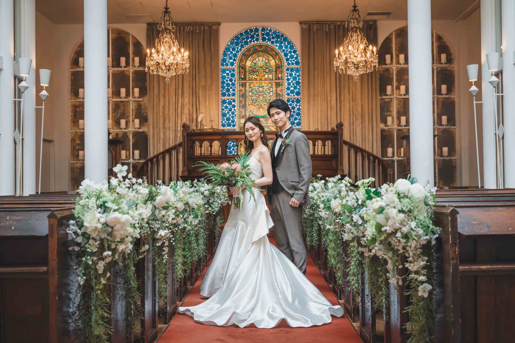 結婚式場でウェディングドレスを着て撮影する白のウェディングドレスを着た新婦様とタキシードを着た新郎様。レッドカーペットで華やかな１枚が撮影できるロケーション地として人気。撮影店舗：STUDIOARC横浜店　神奈川県横浜市中区山下町84-5 メトロタワー山下町 4F