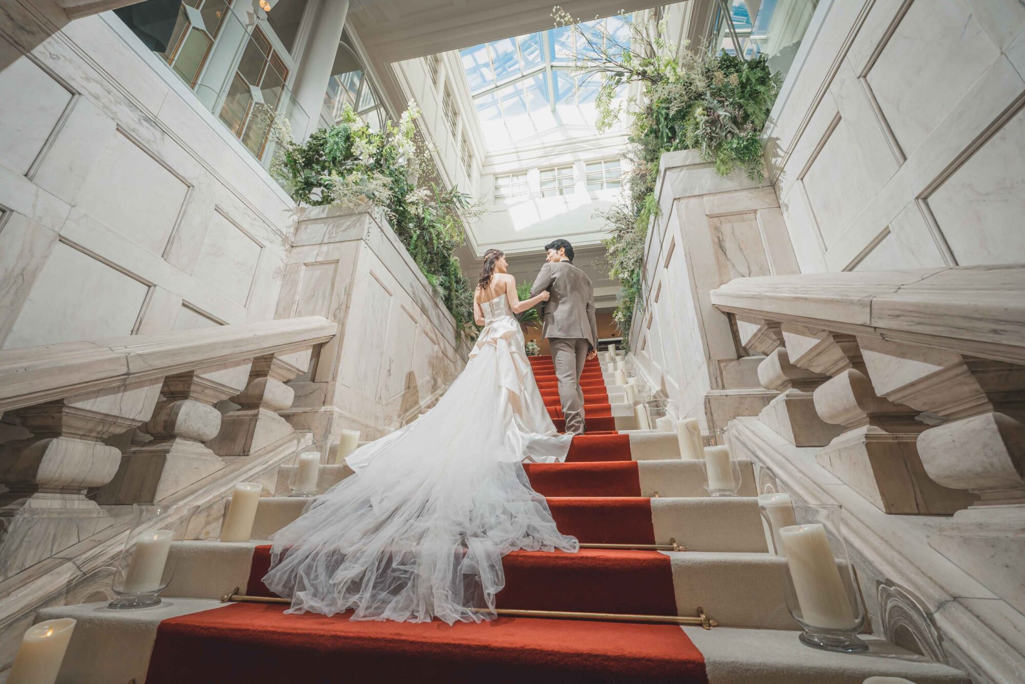 結婚式場でウェディングドレスを着て撮影する白のウェディングドレスを着た新婦様とタキシードを着た新郎様。レッドカーペットの階段で華やかな１枚が撮影できるロケーション地として人気。撮影店舗：STUDIOARC横浜店　神奈川県横浜市中区山下町84-5 メトロタワー山下町 4F