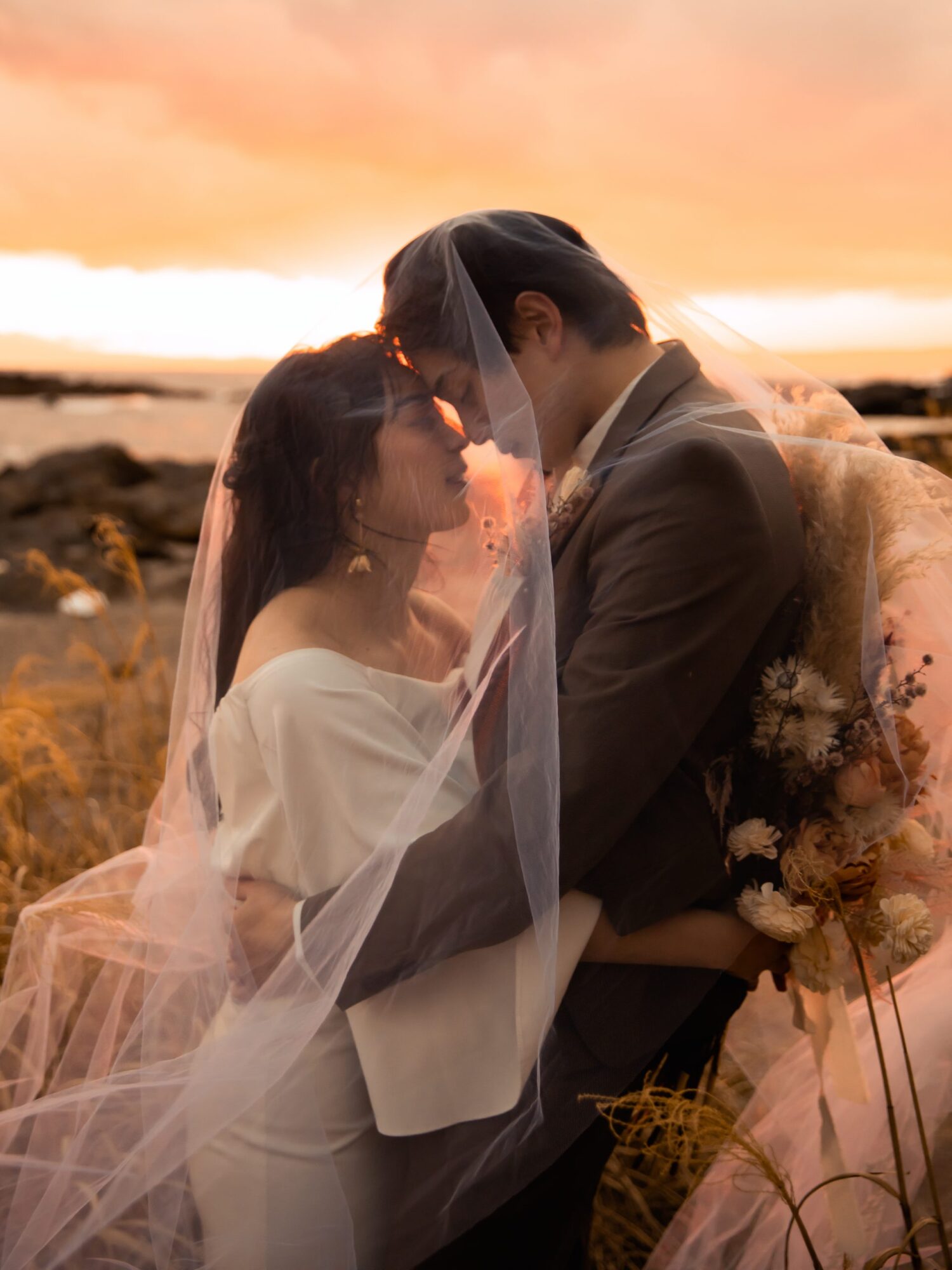 城ケ島でフォトウェディングの撮影をしている新郎新婦様の写真。白のウェディングドレスとタキシードが夕焼けに映える人気のロケーション地。撮影店舗：STUDIOARC横浜店　神奈川県横浜市中区山下町84-5 メトロタワー山下町 4F