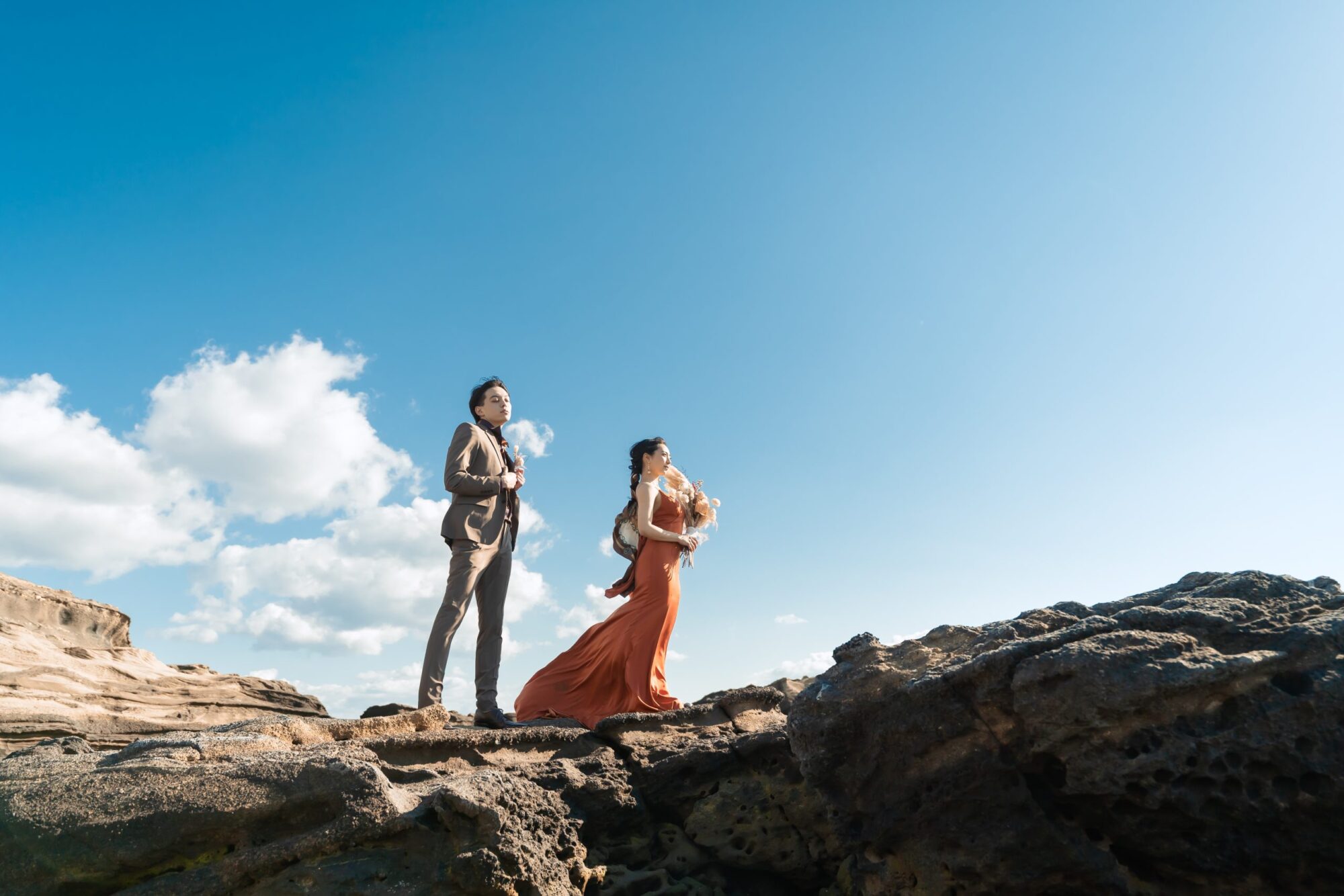 城ケ島でフォトウェディングの撮影をしている新郎新婦様の写真。トレンドのテラコッタのカラードレスとタキシードが青空に映える人気のロケーション地。撮影店舗：STUDIOARC横浜店　神奈川県横浜市中区山下町84-5 メトロタワー山下町 4F