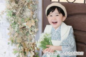 しんかな大阪南店で撮影した七五三の男の子の記念写真。淡いグリーンの着物と白いベストを着て、白い花束を持って笑う姿