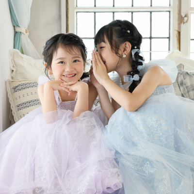 新作チュールドレスを着た二人の女の子。ラベンダー色のドレスを着た子が笑顔で正面を向き、水色のドレスを着た子が耳打ちをしている、写真スタジオでの撮影風景。