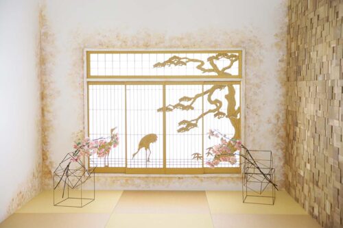 STUDIO ARCセブンパーク天美店の和風の撮影セット。ゴールドの障子窓に鶴と松の木の意匠が描かれ、両脇には梅の花とワイヤーオブジェが置かれている。畳敷きの床と木目調の壁が組み合わさった、格式高く和モダンなスタジオ空間。