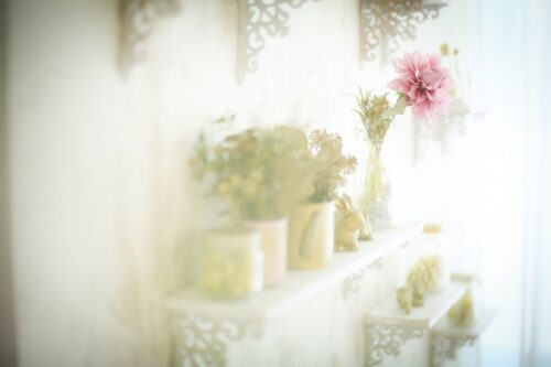 STUDIO ARC枚方店の撮影セット。白い装飾ブラケットの棚に、花瓶に生けた花やうさぎの置物が並び、ピンクのダリアが目を引く、光にあふれた柔らかく優しい雰囲気のスタジオ空間。