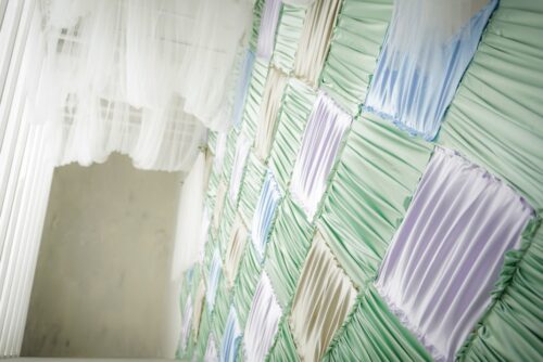 STUDIO ARCららテラスHARUMI FLAG店の店内装飾壁面。グリーン、白、パープル、ブルーの布をパッチワーク状に配置し、ギャザーを寄せたパステルカラーの布壁が奥まで続いており、左手前には白いシアーカーテンが垂れている