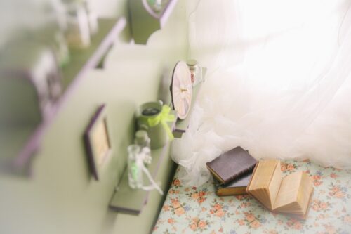 STUDIO ARC錦糸町PARCO店の店内装飾。花柄の布が敷かれた台の上に開かれた古びた本や革製の本が置かれ、傍らには白いチュールのドレスの裾、緑色の棚には小さな時計や瓶などのアンティーク雑貨が並んでいる