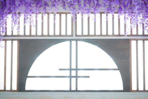 STUDIO ARC 錦糸町PARCO店の和風の撮影セット。上部から紫色の藤の花が垂れ下がり、木製の格子と半円形の大きな窓から自然光が差し込む、和モダンで華やかなスタジオ空間。