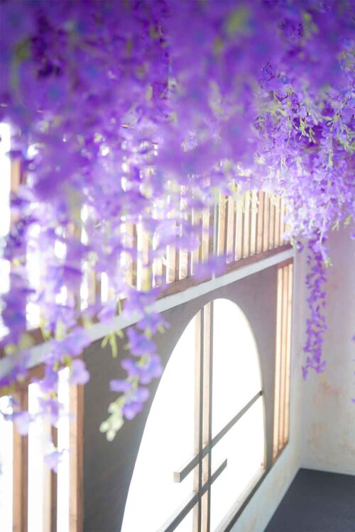 STUDIO ARC 錦糸町PARCO店の和風の撮影セット。手前に紫色の藤の花がたっぷりと垂れ下がり、奥には木の格子と半円形の窓から明るい光が差し込む、華やかで幻想的な和モダンのスタジオ空間。