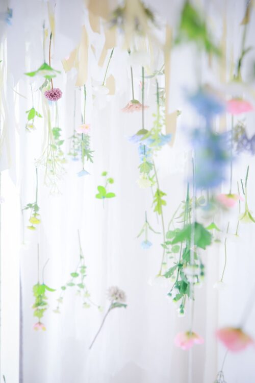 STUDIO ARCイオンモールくみやま店の七五三撮影用の装飾。ピンクや青、白、黄色の小花や葉が糸で天井から逆さに吊るされ、白いカーテンを背景に幻想的な花のカーテンが広がっている