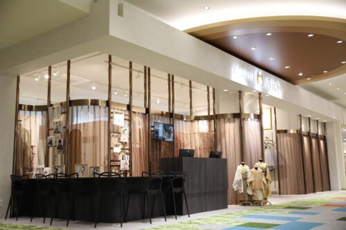 STUDIO ARCららぽーと門真店の店舗外観・入り口。ゴールドの看板が掲げられた店構えに、ブラウン系のカーテンで仕切られたブースが並び、受付カウンターと黒い椅子が設置されている。七五三の着物を着たマネキンも展示された、ショッピングモール内の明るく高級感のある店舗。