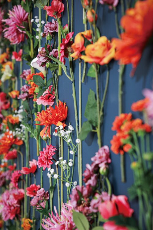 STUDIO ARCららぽーと甲子園店の店内装飾。紺色の壁に、赤やオレンジ、ピンクの花々とかすみ草が縦に並べられ、色鮮やかな花のカーテンのように飾られている