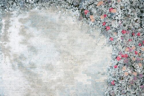 STUDIO ARC横浜店の撮影セット。淡いグレーとベージュのレンガ調の壁を背景に、右側にピンクやサーモンピンクの花とシルバーグリーンの葉が敷き詰められた、シャビーシックで上品な撮影背景。