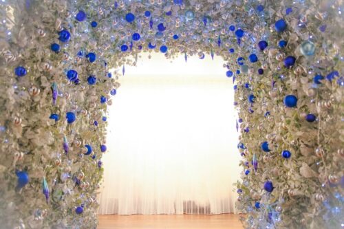STUDIO ARC横浜店の撮影セット。白い花と葉、青やシルバーの丸いオーナメントで飾られたアーチ型の入り口。奥には白いカーテン越しに光が差し込む、幻想的でクリスマスのような煌びやかなスタジオ空間。