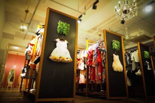 STUDIO ARCセンター北店の衣装レンタルコーナー。木枠のパネルにグリーンの装飾と白いドレスが掛けられ、奥には色とりどりの着物やドレスがずらりと並ぶ、シャンデリアの灯る華やかな店内スペース。七五三やお宮参りに向けた豊富な衣装ラインナップが並ぶ様子がわかる。