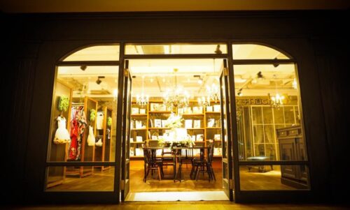STUDIO ARCセンター北店の夜の店舗外観。両開きのガラス扉が開かれ、店内には煌びやかなシャンデリアが灯り、木製の棚に並ぶアルバムやディスプレイされた衣装が見える、温かい光に満ちたエントランス。