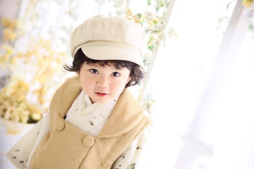 STUDIO ARCで七五三の記念撮影にベージュの被布とキャスケット帽をあわせてカメラを見つめる男の子。