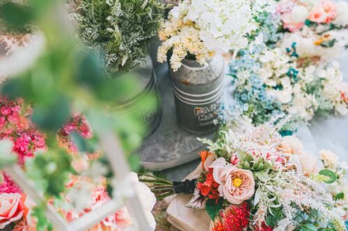 芝Parkside STUDIO店に並ぶ造花のブーケや花材の数々。ピンクや白の花を生けたブリキ缶、色とりどりのバラを束ねたブーケ、白いレース模様の小道具などがテーブルに並べられている様子
