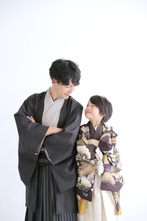 凛々しい着物と袴姿でお揃いのような和装に身を包んだ父親と息子が、腕を組んで見つめ合い微笑む七五三の写真