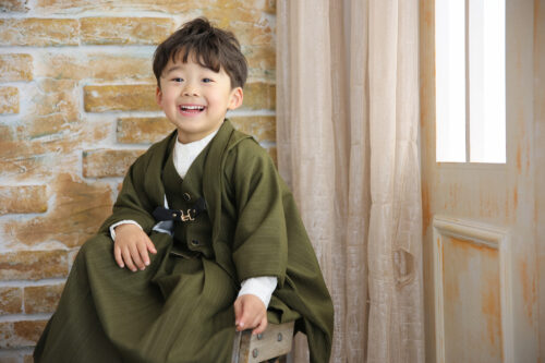七五三3歳の男の子の記念写真。カーキ色のベスト袴姿で椅子に座り、満面の笑顔を見せている