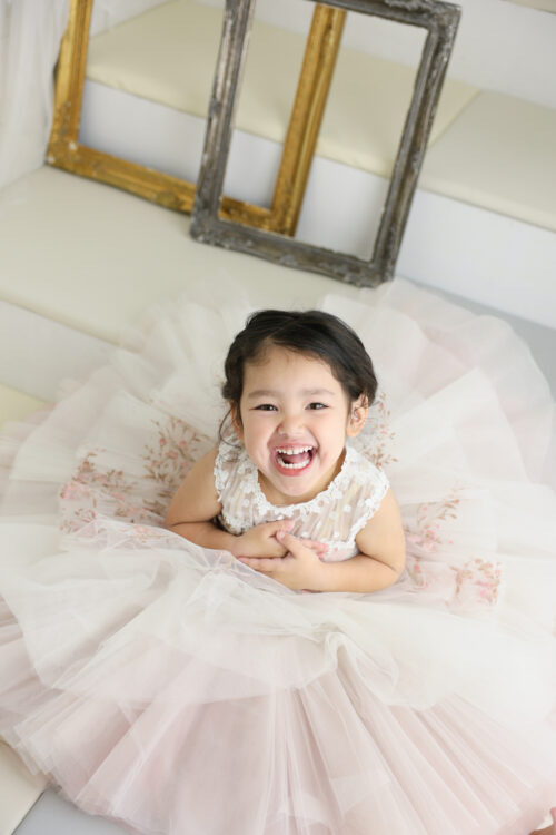 七五三3歳の女の子の記念写真。淡いピンクのチュールドレスを着て、はじけるような笑顔を見せている