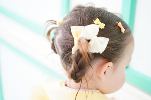 STUDIO ARCららテラスHARUMI FLAG店で撮影した七五三の女の子のヘアアレンジ。編み込みと黄色・オレンジのリボンが施された後ろ姿