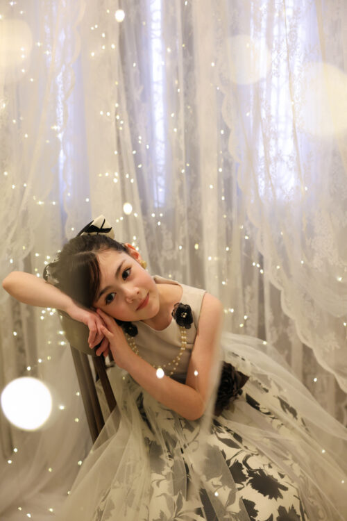 STUDIO ARC心斎橋店で撮影した七五三7歳の女の子の記念写真。白と黒の花柄ドレスに真珠のネックレスを合わせ、椅子にもたれながら微笑んでいる